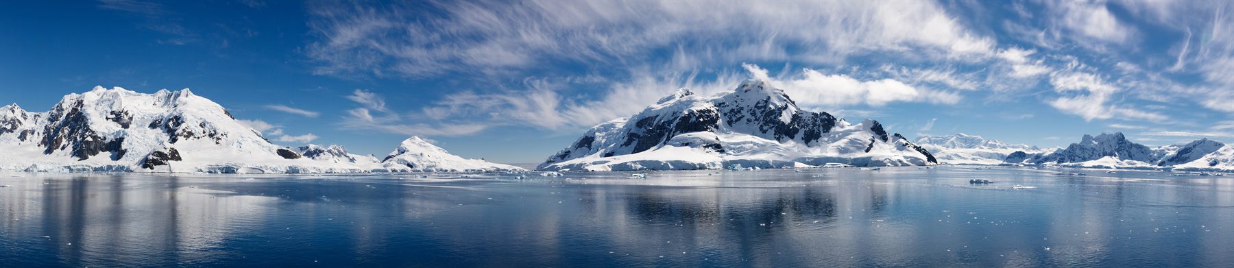 Snow-covered Antarctic peaks reflected in calm water under a blue sky